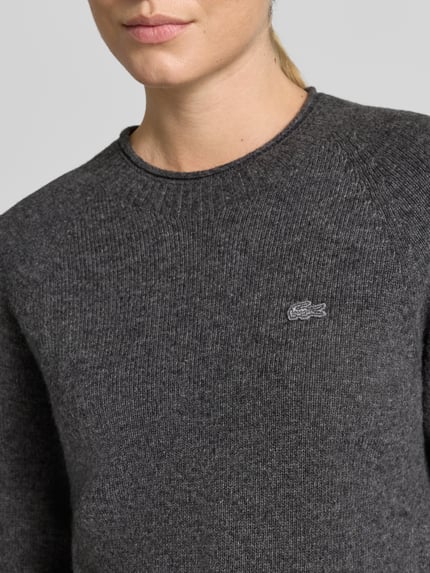 Frauenmodel trägt Regular Fit Pullover aus reiner Wolle von Lacoste, dunkles Grau, feine Strickstruktur, Nahaufnahme Oberkörper, Damen Pullover von Lacoste.