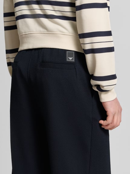 Männermodel trägt Hose mit Strukturmuster und Eingrifftaschen von Emporio Armani in Dunkelblau, Regular-Fit Material-Mix, Nahaufnahme Rückansicht. Material-Mix mit Viskose-Anteil, Bundweite 46 cm, Innenbeinlänge 73 cm, Gesäßtaschen.