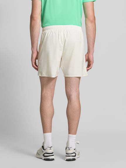 Männermodel trägt Regular Fit Shorts mit integriertem Slip Modell 'ICON' von ASICS TIGER, beige Farbe, elastischer Bund, Ganzkörperansicht Rückansicht. Herren Shorts mit Logo-Print, Bundweite Größe M 37 cm, Innenbeinlänge 18 cm.