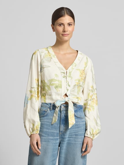 Frauenmodel trägt Cropped Bluse aus Leinen-Viskose-Mix Modell 'SHIRLEY' von Guess mit floralem Muster, V-Ausschnitt, Knopfleiste, Pastelltönen, Nahaufnahme Oberkörper.