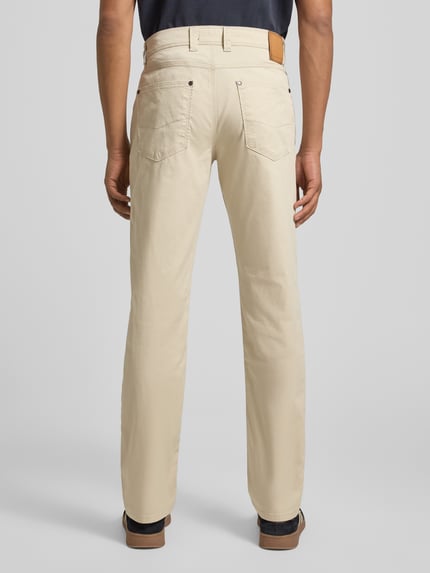 Mężczyzna nosi Hose im 5-Pocket-Design Modell 'CORDOBA' von bugatti, beżowy bawełniany materiał ze stretchem, krój straight fit, widok całej sylwetki z tyłu.