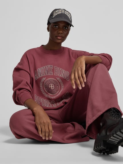 Frauenmodel trägt Regular Fit Sweathose mit Seitenschlitz von Anine Bing in einfarbigem Dunkelrot mit strukturierter Optik und sichtbaren Nähten, elastischer Bund, seitliche Eingrifftaschen, Ganzkörperansicht von vorne.