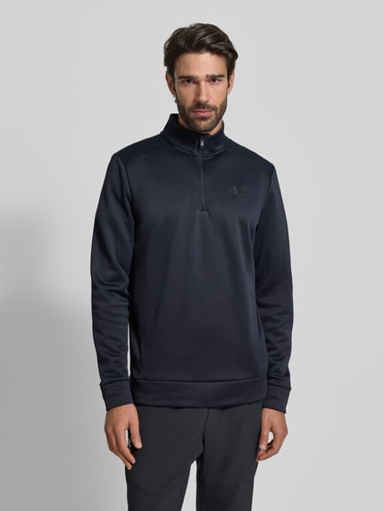 Mannenmodel draagt Sweatshirt mit Label-Detail van Under Armour in donkerblauw, losse pasvorm, hoge kraag, zoom en mouwboorden, voorkant bovenlichaam close-up.