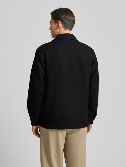 Männermodel trägt Jacke mit Umlegekragen und Knopfleiste Modell 'CAVE' von Forét, schwarzer Baumwoll-Mix, Rückenansicht, Ganzkörperansicht. Regular Fit, Viskose-Anteil, dezente Struktur, neutrale Farben, gerader Schnitt.