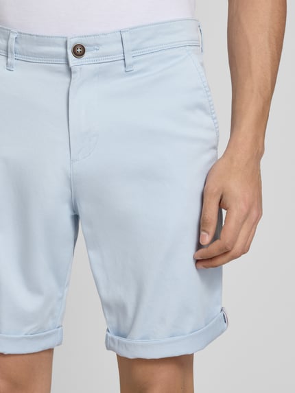 Männermodel trägt Regular Fit Shorts mit Eingrifftaschen Modell 'BOWIE' von Jack & Jones aus Baumwoll-Elasthan-Mix in Hellblau, Nahaufnahme Oberkörper. Bundweite 43 cm, Innenbeinlänge 26 cm, sichtbarer Umschlag, schlicht glatte Oberfläche.