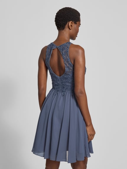 Frauenmodel trägt Cocktailkleid mit floralen Stickereien und Ziersteinen von LAONA, taillierte Passform, Rückenausschnitt, doppellagiger Rock, Ganzkörperansicht Rückansicht.