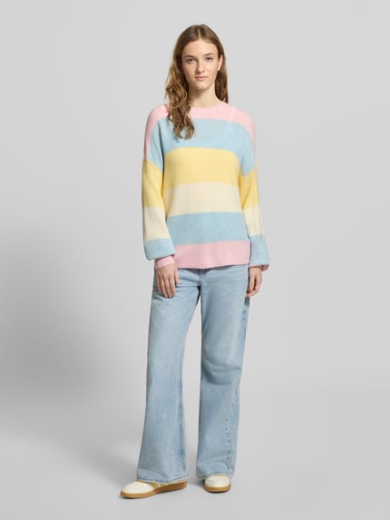 Frauenmodel trägt Regular Fit Strickpullover aus Viskose-Mix Modell 'ATIA' von Only in mehrfarbig gestreifter Optik, Ganzkörperansicht von vorne.