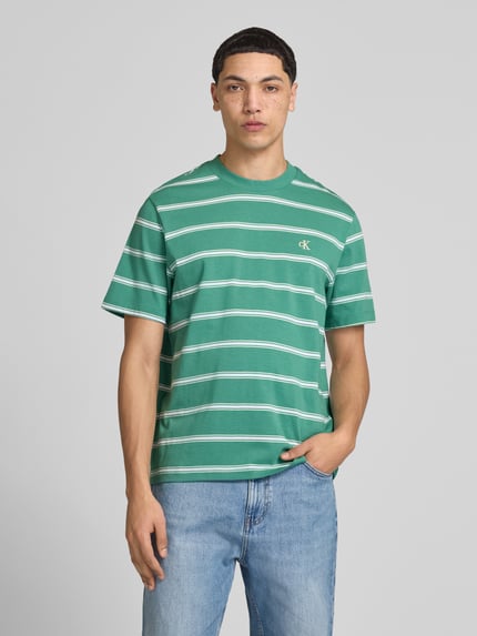 Męski model nosi T-Shirt mit Logo-Stitching od Calvin Klein Jeans, zielony z białymi paskami, czysta bawełna, prosty krój, okrągły dekolt, długość tyłu w rozmiarze M: 69 cm. Ganzkörperansicht z przodu.