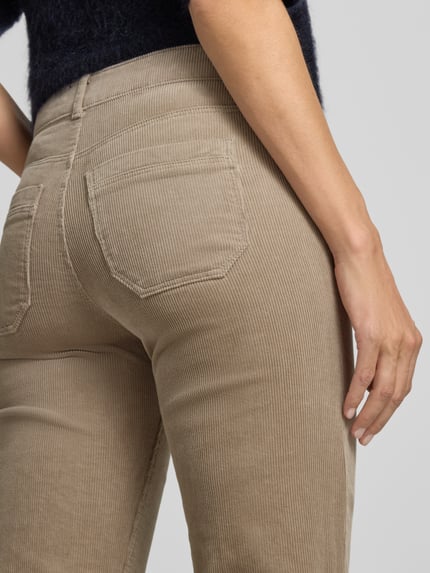 Frauenmodel trägt Cordhose mit aufgesetzten Leistentaschen von Christian Berg Woman, beigefarbener Baumwoll-Mix, Nahaufnahme Rückansicht.