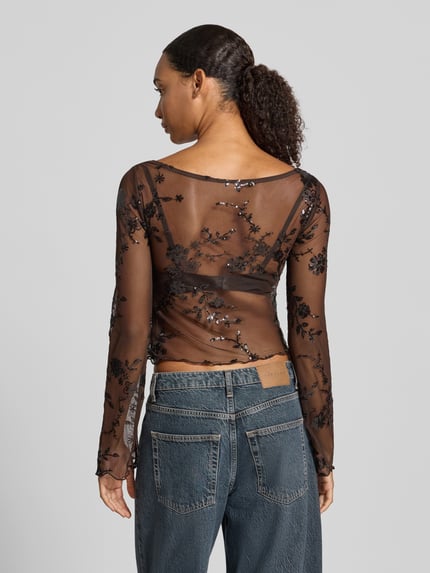 Frauenmodel trägt Langarmshirt mit ausgestelltem Ärmelabschluss von PIECES, schwarzes florales Spitzenmuster auf Mesh, Ganzkörperansicht Rückansicht.