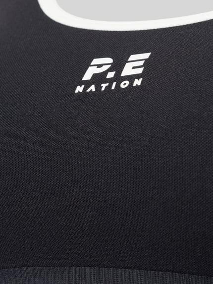 Nahaufnahme Oberkörper, Frauenmodel trägt Sport-BH mit Logo-Print Modell 'ADAPTION SEAMLESS' von P.E Nation, schwarzer Material-Mix mit weißem Logo und feiner Struktur