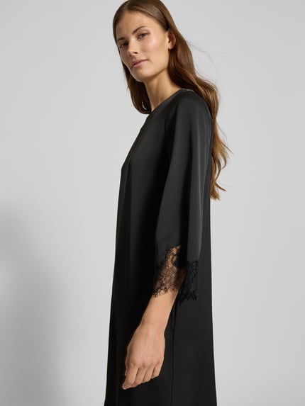 Kobiece model prezentuje sukienkę Knielanges Kleid mit Rundhalsausschnitt Modell 'Dancia' od JOOP!, czarną, z obszyciem koronką, krój relaxed fit, okrągły dekolt, długość do kolan, rękaw o dł. 3/4, widok z boku, ujęcie do pasa.