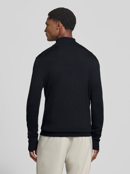 Männermodel trägt Wollpullover mit Rollkragen von Christian Berg Men in Schwarz mit gerippten Abschlüssen, Ganzkörperansicht Rückansicht.