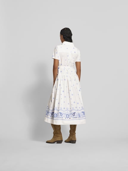 Männermodel trägt Hemdblusenkleid in Midilänge von Self-Portrait in Weiß mit blauen Paisley-Stickereien aus reiner Baumwolle, taillierte Passform, Taillengürtel mit Dornschließe, Szerokość w rozmiarze S: 50 cm, długość całkowita: 127 cm, długość rękawa: 21 cm, Szerokość w talii w rozmiarze S: 55 cm, Ganzkörperansicht Rückansicht