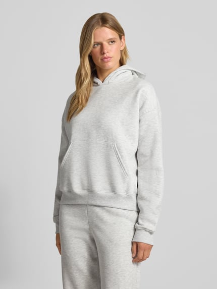 Frauenmodel trägt Relaxed Fit Hoodie aus Baumwoll-Mix Modell 'Iconic' von Gina Tricot in Hellgrau mit Känguru-Tasche, Ganzkörperansicht von vorne.