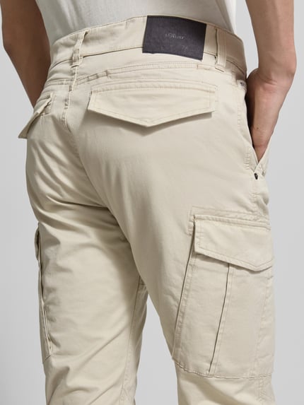 Mannelijk model draagt Regular Fit cargobroek uit katoenmix van s.Oliver RED LABEL in effen kleuren met cargozakken, labelpatch, studdetail, riemlussen, achterzakken, steekzakken, detailopname achterzijde.