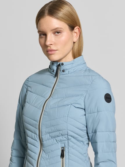 Frauenmodel trägt Slim Fit Jacke in Stepp-Optik von G.I.G.A. DX in Hellblau mit Reißverschlüssen und Logo-Detail, Nahaufnahme Oberkörper. Rückenlänge, Schulterbreite, Brustweite und Ärmellänge wie bei Größe 36 aus dem Kontext.