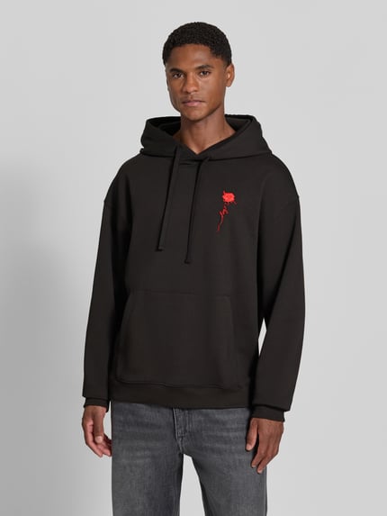 Männermodel trägt Regular Fit Hoodie aus reiner Baumwolle Modell 'Diflowhood' von HUGO in Schwarz mit rotem Detail, Ganzkörperansicht von vorne, Herren Hoodie von HUGO.