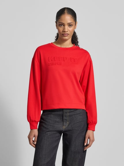Vrouwenmodel draagt Sweatshirt mit Viskose-Anteil van monari in felrood met ronde hals en statementreliëf, losse fit, elastische mouwboorden, vooraanzicht bovenlichaam.