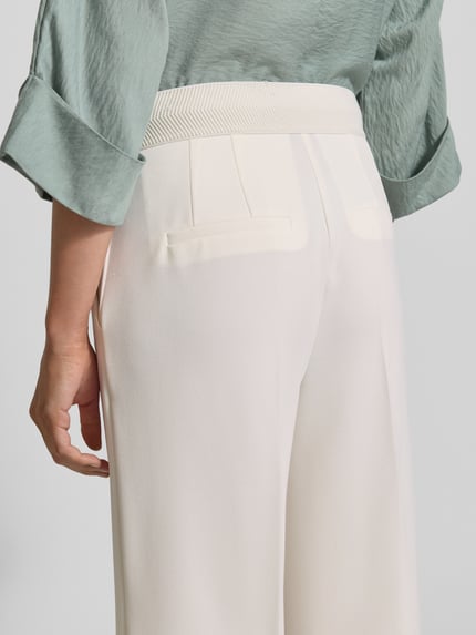 Frauenmodel trägt Wide Fit Stoffhose mit Bügelfalten Modell 'Juli' von Betty Barclay in Creme, elastischer Material-Mix, Detailaufnahme Rückansicht.