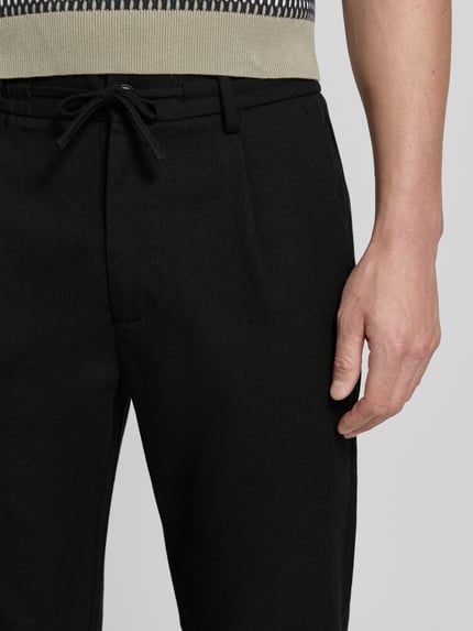 Männermodel trägt Slim Fit Stoffhose mit Viskose-Anteil von Lindbergh, Schwarz, Elastischer-Material-Mix, Strukturmuster, Nahaufnahme Oberkörper.