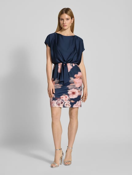 Vrouwenmodel draagt knielanges Cocktailjurk met knoopdetail van SWING, materiaalmix met stretch, recht model, knielengte, ronde hals, bloemenprint. Ganzlichaamsaanzicht van voren.