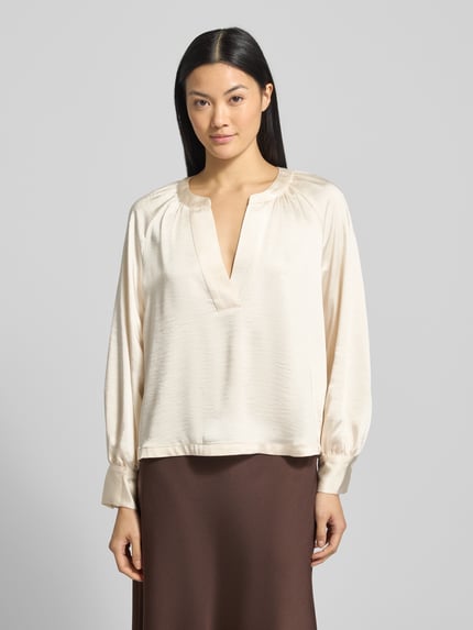 Frauenmodel trägt Oversized Blusentop mit Cacharel-Falte von s.Oliver RED LABEL, Optik: Unifarben, Passform: Oversized, Tiefer V-Ausschnitt, Langarm mit Manschette, abgerundeter Rumpfabschluss, glatte Textur in Creme, Ganzkörperansicht von vorne.