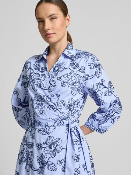 Frauenmodel trägt Wickelkleid mit Stitchings und 3/4-Arm von WHITE LABEL in Hellblau mit floralen Mustern, Nahaufnahme Oberkörper. Damen, A-Linie, Midikleid, Hemdblusenkragen, V-Ausschnitt, Bindegürtel, Rückenlänge bei Größe 36: 116 cm, Brustweite: 48 cm, Ärmellänge: 45 cm.