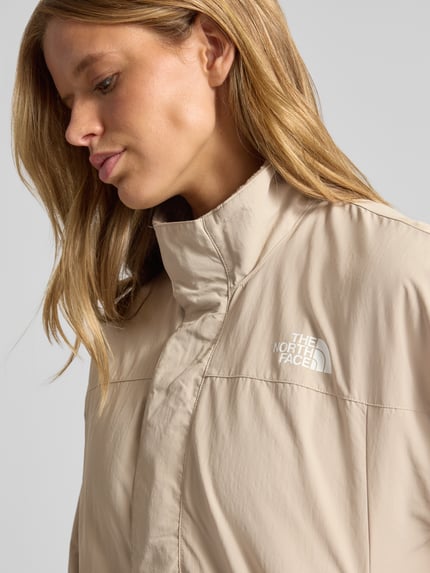 Frauenmodel trägt Jacke mit Wendefunktion Modell 'YUMIORI' von The North Face in Beige, glatte Textur, Logo auf Brust, Nahaufnahme Oberkörper. Regular Fit, Stehkragen, Damen Jacke, Rückenlänge 62 cm, Schulterbreite 52 cm, Brustweite 57 cm, Ärmellänge 57 cm.