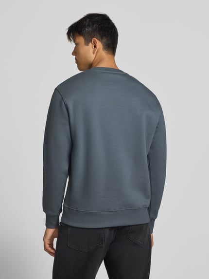 Männermodel trägt Sweatshirt mit Label-Details von Alpha Industries aus Baumwoll-Mix mit gerippten Abschlüssen, Ganzkörperansicht Rückansicht.