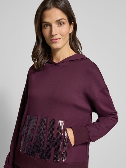 Frauenmodel trägt Hoodie aus Viskose-Mix mit Känguru-Tasche und Pailletten von Milano Italy, Relaxed-Fit, violett, Nahaufnahme Oberkörper.