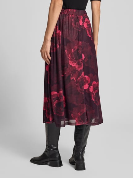 Frauenmodel trägt Glockenrock mit elastischem Bund Modell 'Se44renity' von ZABAIONE, Midilänge, rotes Blumenmuster, Ganzkörperansicht Rückansicht. Material-Mix mit Stretch-Anteil, A-Linie, Damenrock.