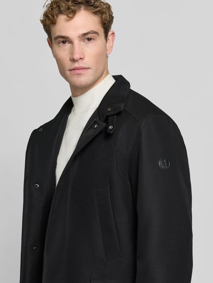 Männermodel trägt Kurzmantel mit Stehkragen Modell 'DARRY' von JOOP!, einfarbig, strukturierte Webware, Logo-Patch, Nahaufnahme Oberkörper.
