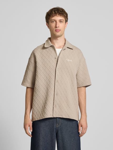 Männermodel trägt Modern Fit Freizeithemd mit Logo-Stitching Modell 'Jovren' von Pegador im Strukturmuster, Kentkragen, Knopfleiste, Material-Mix, beige, Ganzkörperansicht von vorne.