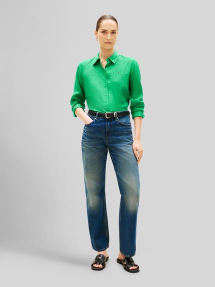 Vrouwenmodel draagt Relaxed Fit Langarmbluse aus reinem Leinen van Tommy Hilfiger in effen groen, overhemdkraag, logostitching, knoopsluiting, manchet, afgeronde rompzoom, gevlamd garen, materiaal: linnen. Ganzkörperansicht van voren.