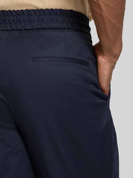 Männermodel trägt Slim Fit Bundfaltenhose aus Baumwoll-Mix Modell 'GETLIN251F3' von HUGO in Dunkelblau, Detailaufnahme Rückansicht.