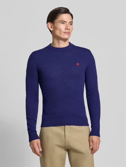Männermodel trägt Slim Fit Strickpullover aus reiner Wolle mit Label-Stitching von MCNEAL, marineblau, gerippte Abschlüsse, Ganzkörperansicht von vorne.