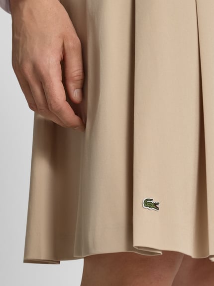 Frauenmodel trägt A-Linie Midi-Rock aus Baumwoll-Mix von Lacoste in Beige mit glatter Struktur und gesticktem Logo, Nahaufnahme Oberschenkel. Damen Midi-Rock von Lacoste.