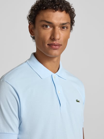 Męski model nosi Koszulkę polo z wyhaftowanym logo Model 'L.12.12 CORE' od Lacoste, bawełna, jednokolorowy, krój regular fit, kołnierzyk polo, listwa guzikowa, prążkowane zakończenia rękawów, długość tyłu 72 cm, rozmiar M, jasnoniebieski, z przodu, zbliżenie górnej części ciała.