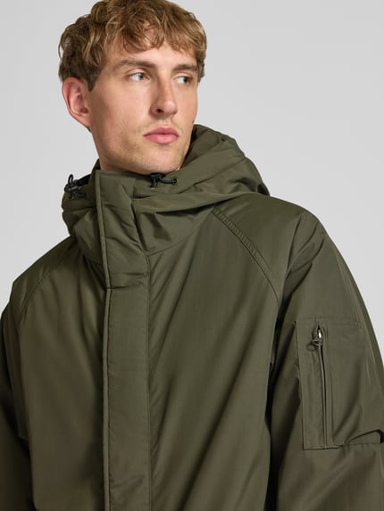 Männermodel trägt olivgrünen Parka mit Pattentaschen Modell 'Stanwood' von Carhartt Work In Progress, Reißverschluss, Nahaufnahme Oberkörper.