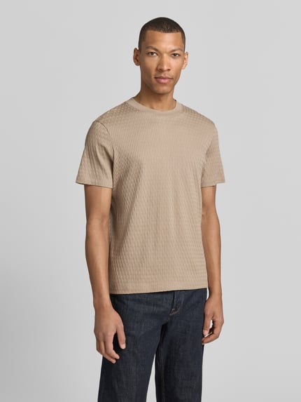 Männermodel trägt T-Shirt mit Strukturmuster Modell 'Raulos' von JOOP! Collection aus reiner Baumwolle, Modern Fit, Rundhalsausschnitt, Label-Detail, beige, Ganzkörperansicht von vorne.
