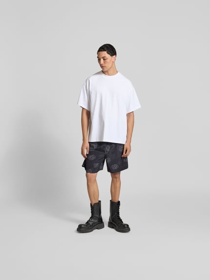 Männermodel trägt Shorts aus reiner Viskose von Officine Générale in Schwarz mit Print, elastischem Bund und Tunnelzug, Ganzkörperansicht von vorne.