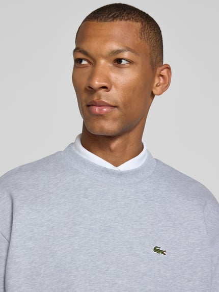 Männermodel trägt Regular Fit Sweatshirt aus Baumwoll-Mix von Lacoste in Hellgrau, feine Struktur, dezentes Logo, Nahaufnahme Oberkörper. Herren Sweatshirt von Lacoste.