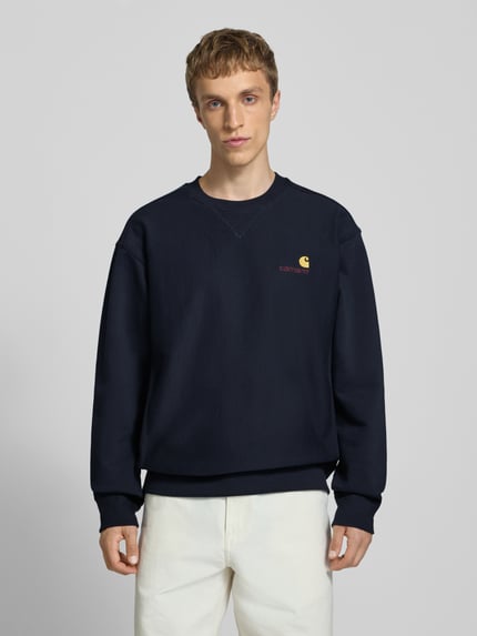 Männermodel trägt Regular Fit Sweatshirt mit Logo-Stitching von Carhartt Work In Progress in Dunkelblau, Baumwoll-Mix, Rundhalsausschnitt, elastische Abschlüsse, Ganzkörperansicht von vorne.
