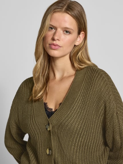 Frauenmodel trägt Boxy Fit Strickjacke mit V-Ausschnitt Modell 'CAROL' von ONLY in Olive, grobe Strickstruktur, Damen Strickjacke, Nahaufnahme Oberkörper.