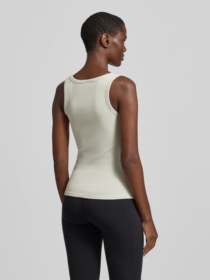 Vrouwenmodel draagt Slim Fit Top uit viscosemix model 'Colette' van Guess Activewear, elastisch, logo-applicatie, ronde hals, ruglengte maat S 51 cm, achteraanzicht, volledige lichaamsopname.