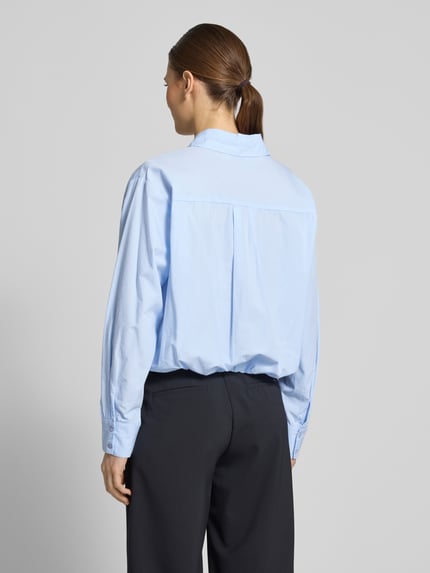Vrouwenmodel draagt Cropped blouse met overhemdkraag model 'Emmana' van Neo Noir in lichtblauw puur katoen, ruglengte 53 cm, mouwlengte 57 cm, knoopsluiting, geheel van achteren gezien.