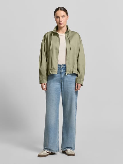 Kobiece modelka nosi Jacke aus Lyocell-Baumwoll-Mix Modell 'Jarusa' od OPUS, oliwkowa z nadrukowaną fakturą, krój relaxed fit, stójka z troczkiem, zamek błyskawiczny, długość tyłu w rozmiarze 36: 56 cm, szerokość ramion w rozmiarze 36: 54 cm, szerokość w biuście w rozmiarze 36: 57 cm, długość rękawa w rozmiarze 36: 53 cm, pełny widok z przodu