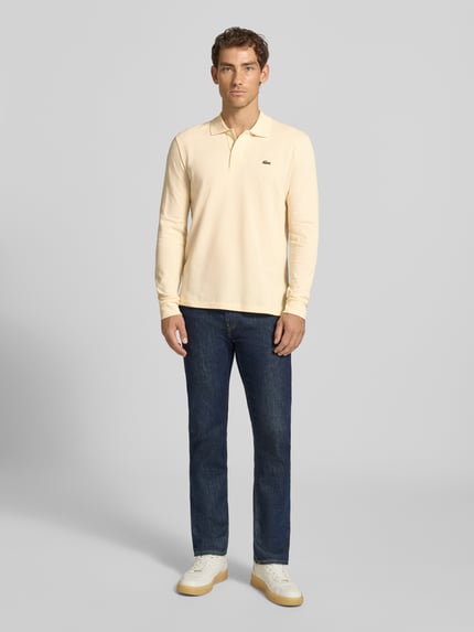 Männermodel trägt Regular Fit Poloshirt aus reiner Baumwolle von Lacoste in Hellgelb, kombiniert mit Jeans, Ganzkörperansicht von vorne.