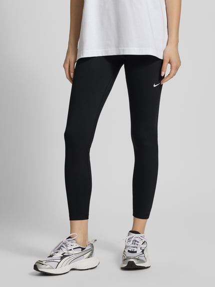 Frauenmodel trägt Leggings mit elastischem Bund und Logo von NIKE TRAINING, Material-Mix mit Stretch-Anteil, Körpernahe Passform, Nahaufnahme Unterkörper.